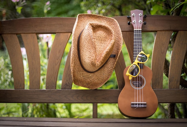 Foto ukulele de verão com óculos de sol amarelos em um banco de parque de madeira