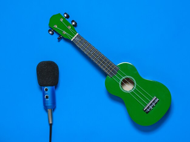 Foto ukulele e microfone azul com fio sobre fundo azul.