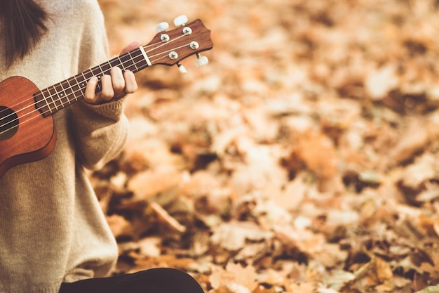 Ukulele em mãos de mulher se aproximando tocando um instrumento acústico ukulele no outono ao ar livre com foto tonificada de espaço de cópia