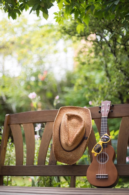 Ukulele de verano con gafas de sol amarillas en un banco del parque de madera