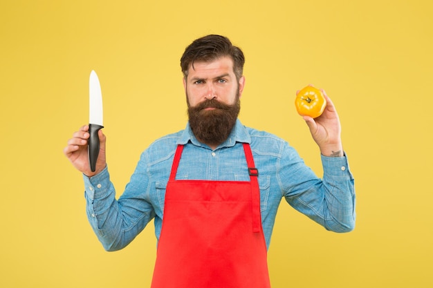 Ultimative Liste der Schneidetechniken, die jeder Koch kennen sollte. Bärtiger Mann bereitet Tomaten zu. Der Koch bereitet das Essen zu. Sicheres Schneiden. Gemüse schneiden. Rezept für frischen Salat. Reifer Mann hält Messer und Gemüse.