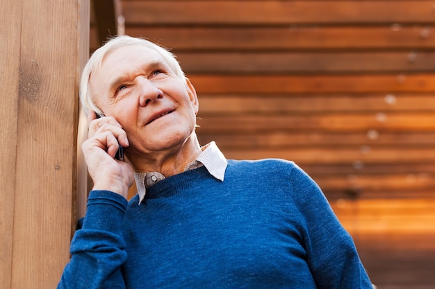 Último homem ao telefone. homem sênior feliz falando no celular e sorrindo enquanto fica ao ar livre