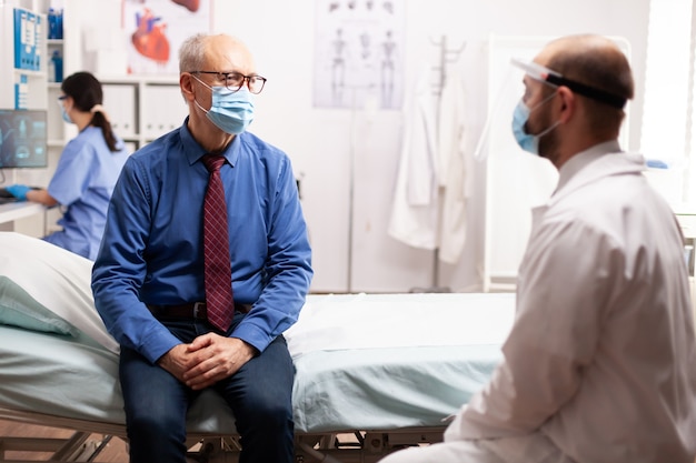 Último homem conversando com o médico sobre o tratamento sentado na cama protegendo a máscara facial como medida de segurança durante a gravidez 19