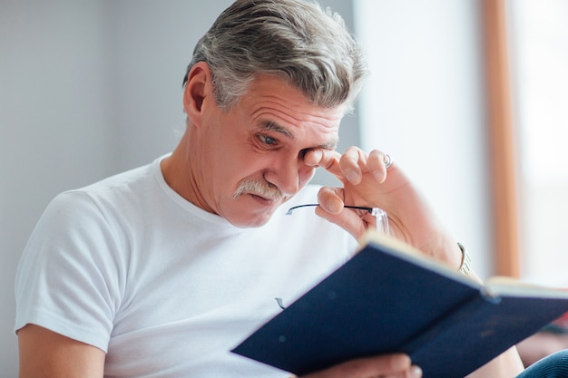 Último homem é educado e tem ler um livro, relaxado no sofá na sala de estar.