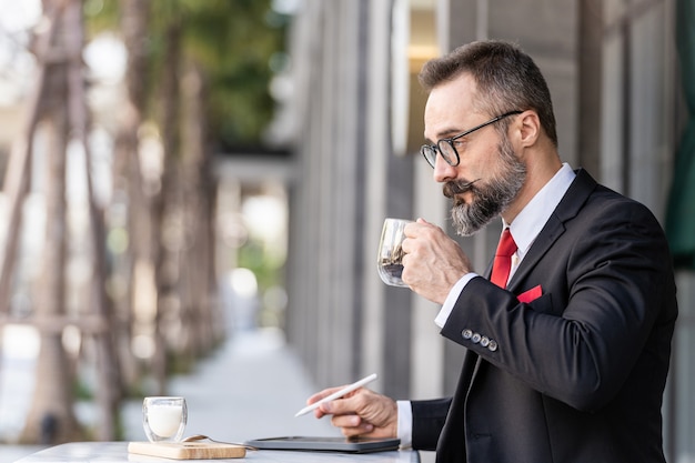 Último homem em terno de negócio inteligente pensando e sentado na mesa de centro ao ar livre.