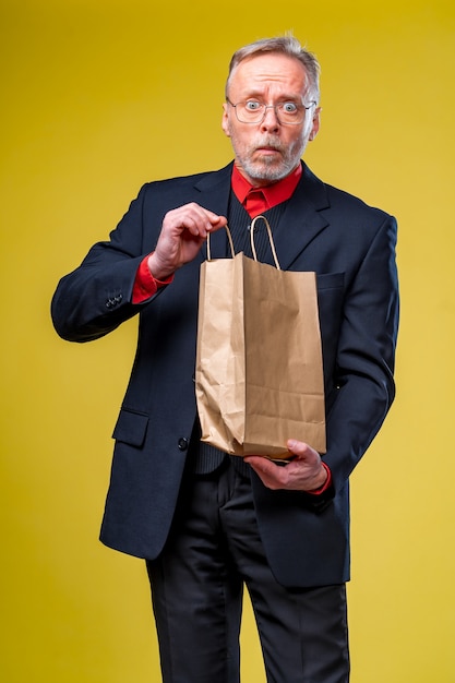 Último homem está olhando para um saco de papel recebendo um presente. eco compras. homem de terno em fundo amarelo.