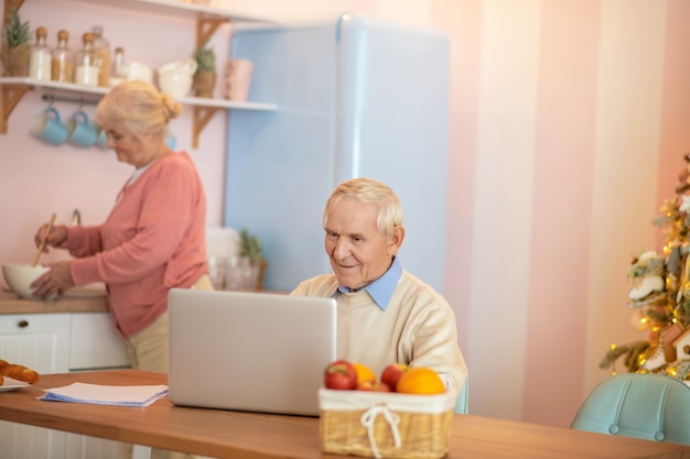 Último homem trabalhando em um laptop enquanto sua esposa cozinha