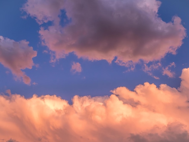 Los últimos rayos del sol al atardecer iluminan un grupo de nubes naranjas en la parte inferior y nubes oscuras en la sombra en la parte superior con un cielo azul oscuro de fondo.