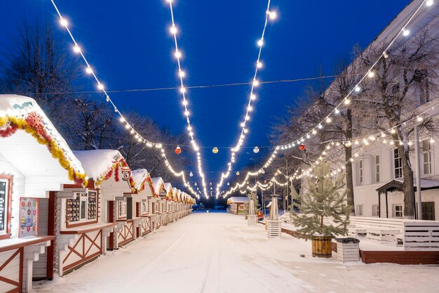 Ulyanovsk Rússia 14 de fevereiro de 2022 Casas de madeira de Ano Novo decoradas com guirlandas e enfeites em uma manhã gelada e nevada Rua coberta de neve em decorações de Natal