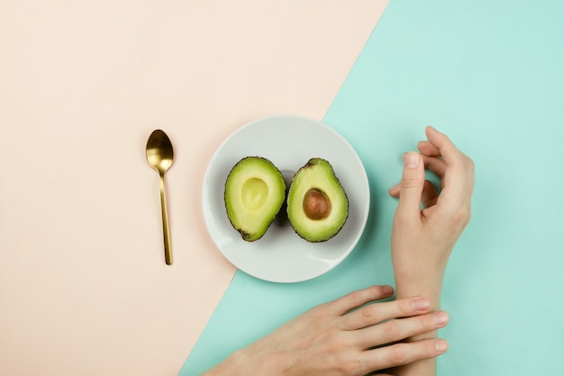 Um abacate cortado em um prato branco ao lado das mãos de alguém