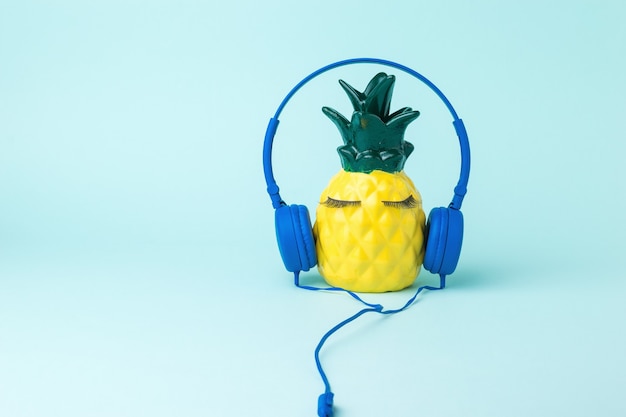 Um abacaxi amarelo feliz em fones de ouvido azuis sobre um fundo azul. O amor pela música.