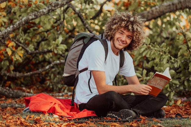 Um adolescente afro relaxa enquanto lê um livro enquanto está sentado na floresta em um belo clima de outono