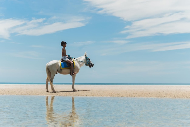 Um adolescente anda a cavalo na praia.