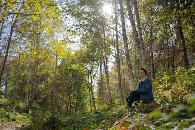 Foto um adolescente atencioso sentado na floresta durante o outono