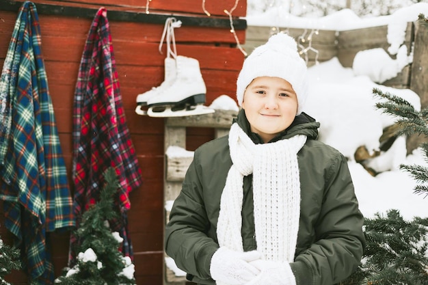 Um adolescente bonito com chapéu branco tricotado fica na varanda da casa de campo e decora a árvore de natal para