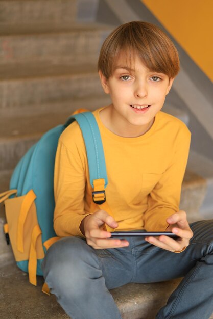 Um adolescente feliz em uma camiseta amarela senta-se com um telefone perto da parede amarela usando tecnologia online