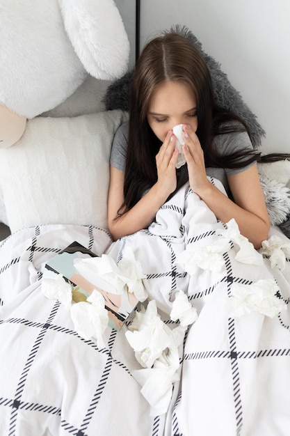 Um adolescente frio rasga o nariz num lenço o tempo todo debaixo de um edredom quente.