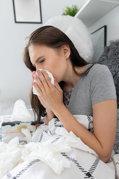 Um adolescente frio rasga o nariz num lenço o tempo todo debaixo de um edredom quente.