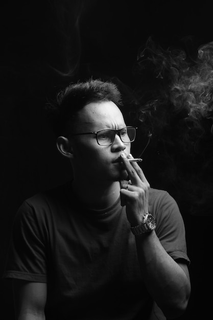 um adolescente fumando em um fundo preto e fumando na sala do estúdio fotográfico