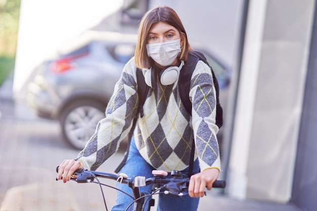 um adolescente indo para a escola de bicicleta e usando uma máscara facial devido à pandemia de coronavírus