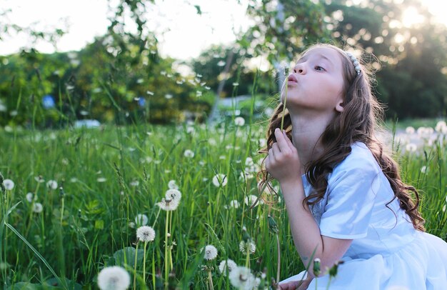 Um adolescente soprando sementes de uma flor dente-de-leão em um parque na primavera