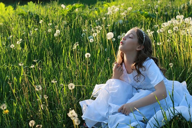 Um adolescente soprando sementes de uma flor dente de leão em um parque na primavera