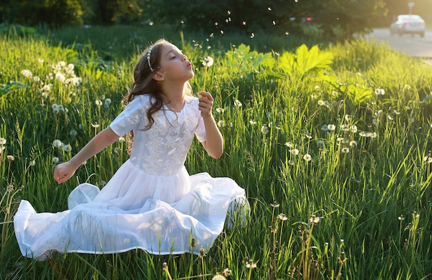 Um adolescente soprando sementes de uma flor dente de leão em um parque na primavera