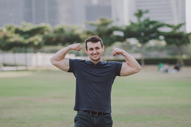 Um adulto jovem e sorridente atleta de fitness mostra os braços estendidos e os bíceps flexíveis