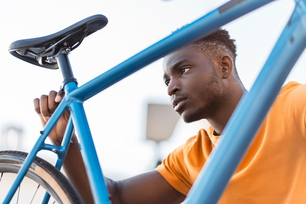 Um africano atraente a verificar o assento de uma bicicleta na rua.