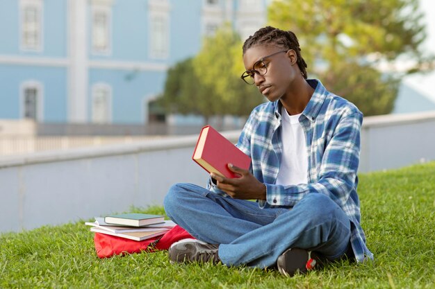 Um afro-americano atencioso com um livro ao ar livre no parque do campus.