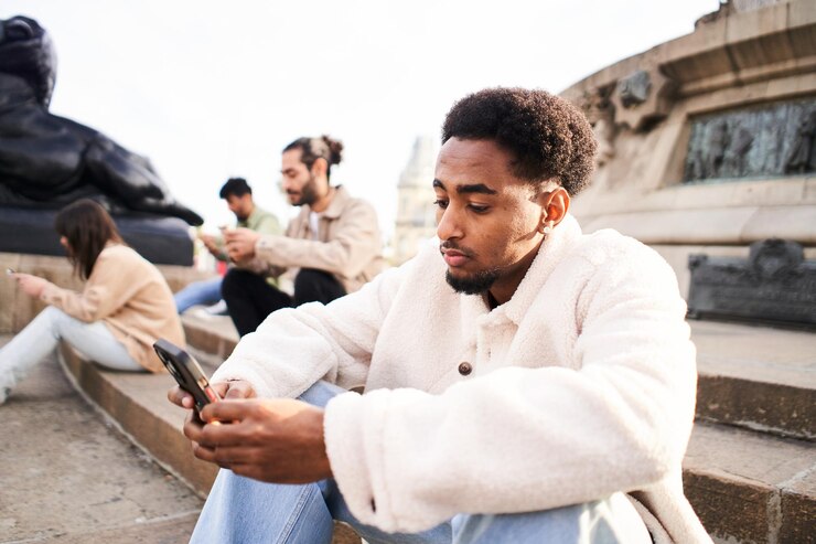 Foto um afro-americano com um telemóvel sentado nas escadas de uma cidade com outros amigos ignorando-se uns aos outros usando smartphones um grupo de viciados em tecnologia