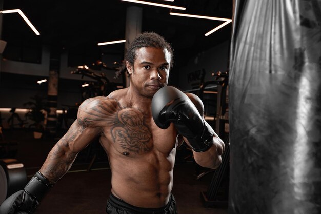 Um afro-americano treina em uma academia e fecha os punhos em seu saco de boxe. Conceito de: ginásio, fitness, boxe, sucesso, treino e potência.