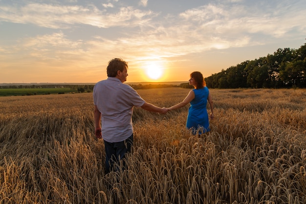 Um agricultor adulto e sua esposa estão caminhando de mãos dadas pelo campo de trigo.