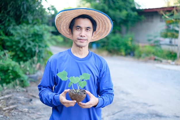 Um agricultor asiático vestido de azul está de pé segurando uma muda para plantar