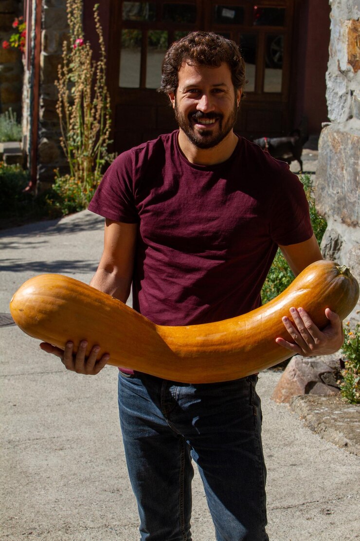Foto um agricultor com barba segura uma abóbora amarela alongada