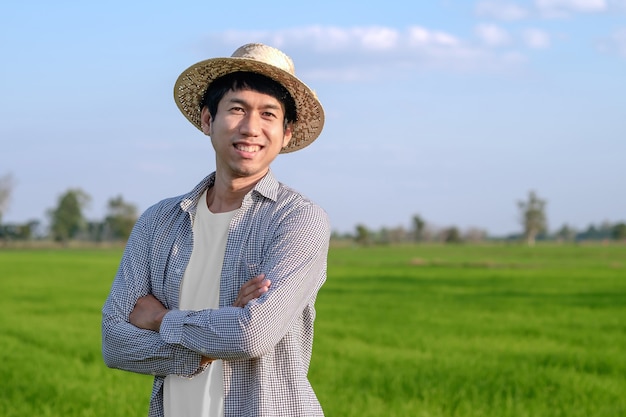 Um agricultor com um chapéu tecido está de pé com os braços cruzados e sorrindo no campo.