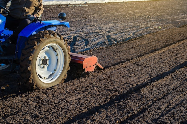 Um agricultor em um trator cultiva um campo agrícola Suavizando o solo e preparando-se para cortar fileiras para a próxima temporada de sementeira na primavera Cultivo de terras Pequenas fazendas Trabalho na indústria agrícola