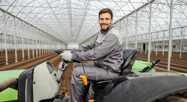 Um agrônomo está sentado no trator e cultivando a terra em estufa