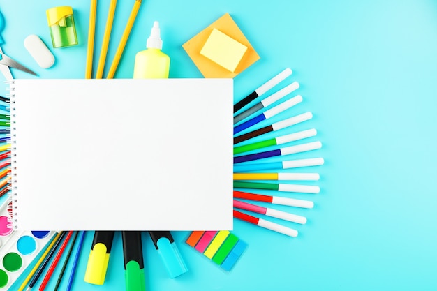 Um álbum para o desenvolvimento criativo na escola, com papel timbrado sobre fundo de cianeto. Uma paleta de tintas coloridas, marcadores, pincéis e lápis.