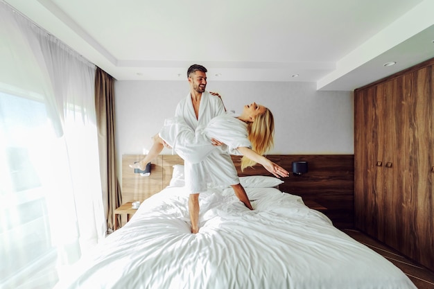 Foto um alegre casal de meia-idade em roupões de banho comemorando seu aniversário em um hotel. um homem segurando uma mulher nas mãos.