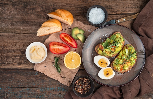 Um almoço leve de sanduíches com abacate e tomate com alecrim em fundo de madeira. Vista superior com espaço de cópia. O conceito de alimentação saudável.