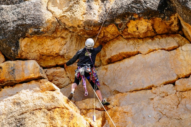 Foto um alpinista com uma corda de segurança subindo em uma rocha plana com rachaduras e ranhuras na superfície