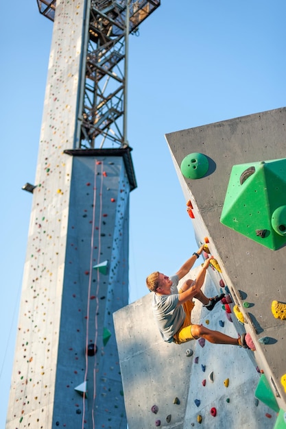 Um alpinista masculino está escalando ao ar livre em uma pedra artificial sem cinto de segurança