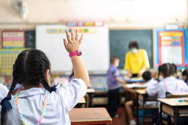 Foto um aluno do ensino fundamental está levantando as mãos para perguntar ao professor em frente à classe bangkok