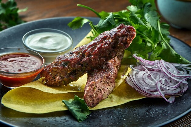 Um apetitoso prato da culinária turca - kebab de frango de carne picada com pão sírio, coentro, cebola e molhos, servido em um prato azul sobre uma mesa de madeira. comida do restaurante. vista de perto