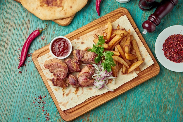 Um apetitoso prato oriental - frango grelhado ou kebab de carne com acompanhamento de batatas e cebolas com cebolas vermelhas sobre uma mesa verde. Cozinha georgiana. Shish kebab