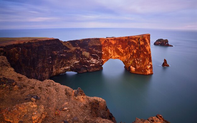 Foto um arco de rocha está na água perto do oceano.