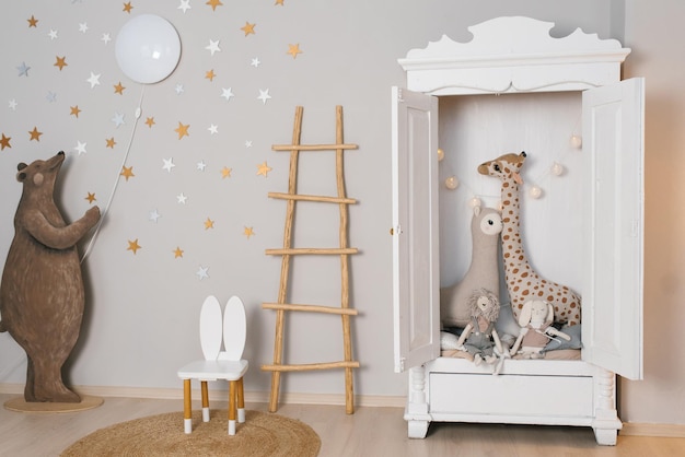 Um armário branco com um animal de pelúcia de girafa dentro da sala das crianças é decorado com estrelas e uma escada