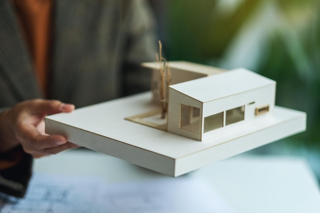 Um arquiteto segurando e trabalhando em um modelo de casa de arquitetura com papel de desenho de loja no escritório