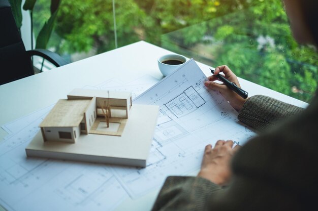 Um arquiteto trabalhando em um modelo de casa de arquitetura com papel de desenho de loja no escritório